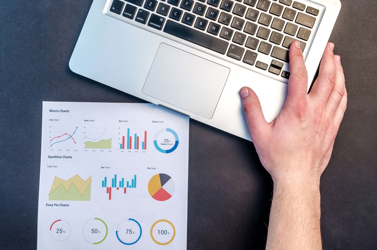 Vue plongeante d’un espace de travail professionnel avec un ordinateur portable et des graphiques de données colorés sur papier.